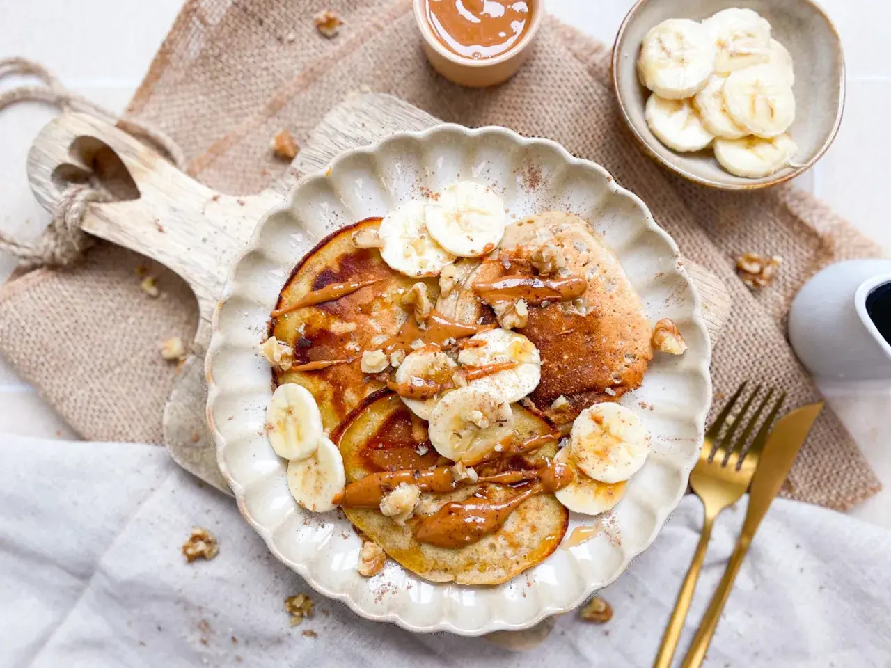 Bananen Pancakes ohne Ei, garniert mit Bananenscheiben, Walnüssen und einer cremigen Sauce. Ein köstlicher Start in den Tag.