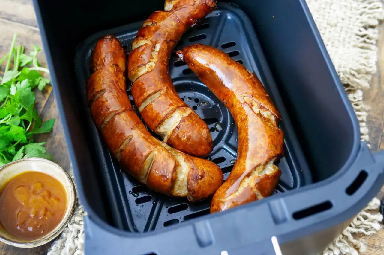 Drei goldbraune Bratwürste in der Heißluftfritteuse, bereit für leckere Bratwurst Rezepte. Dazu ein Schälchen mit Sauce und frische Petersilie.