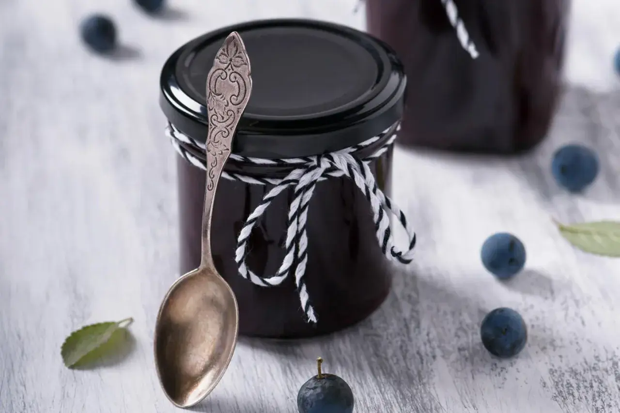 Glas mit Schlehenmarmelade, Löffel und Schlehen. Perfekt für Schlehen Rezepte.