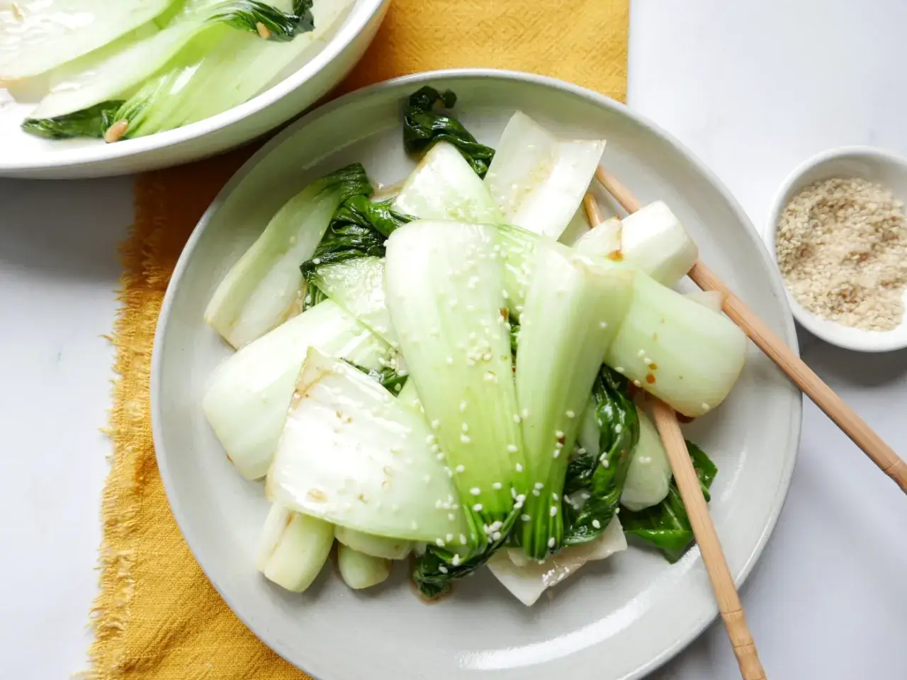 Gebratener Pak Choi mit Sesam bestreut, serviert mit Stäbchen.