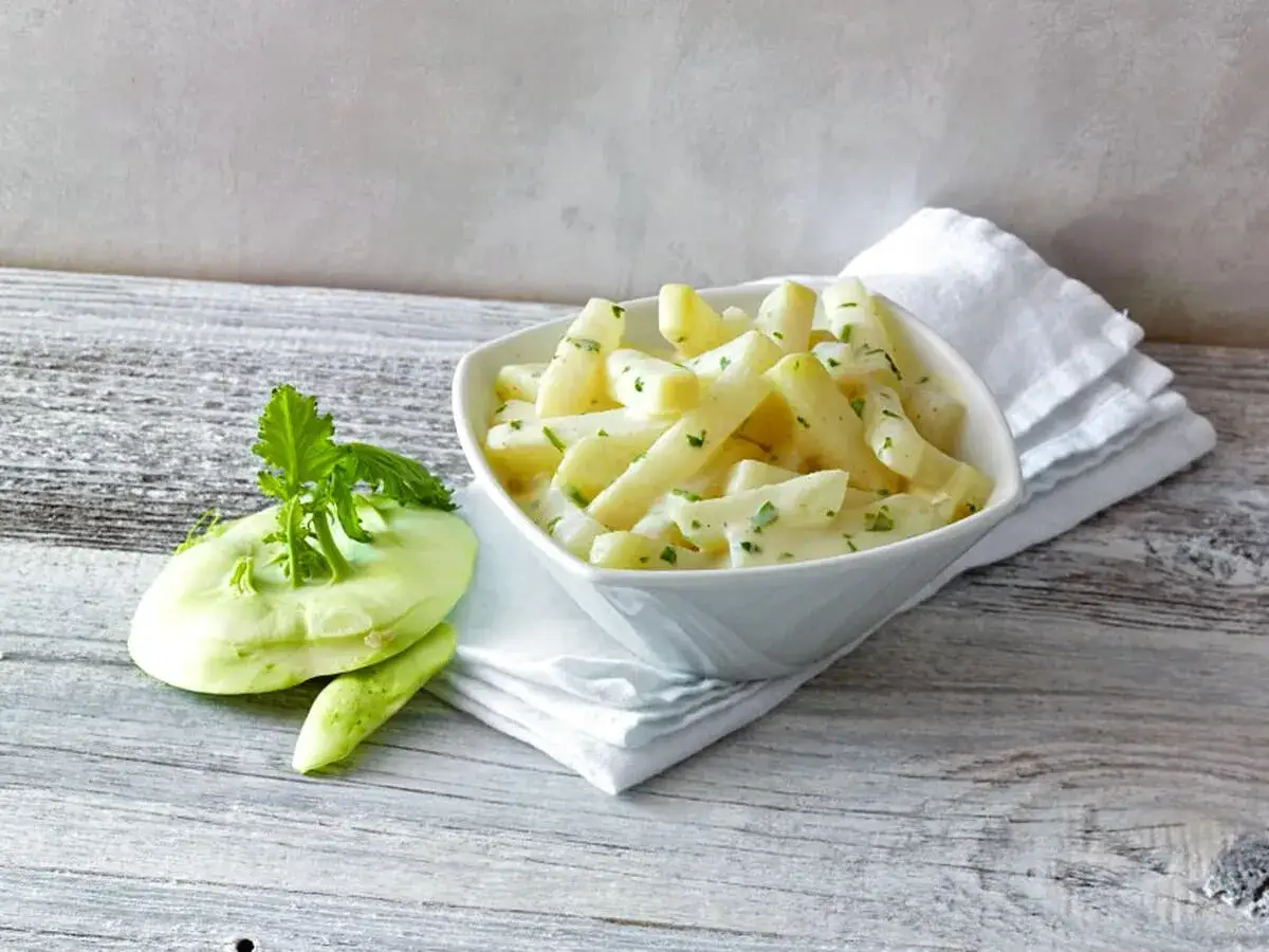 Kohlrabi kochen: Ein cremiges Gericht mit Kohlrabi-Stiften und frischer Petersilie, daneben ein roher Kohlrabi.