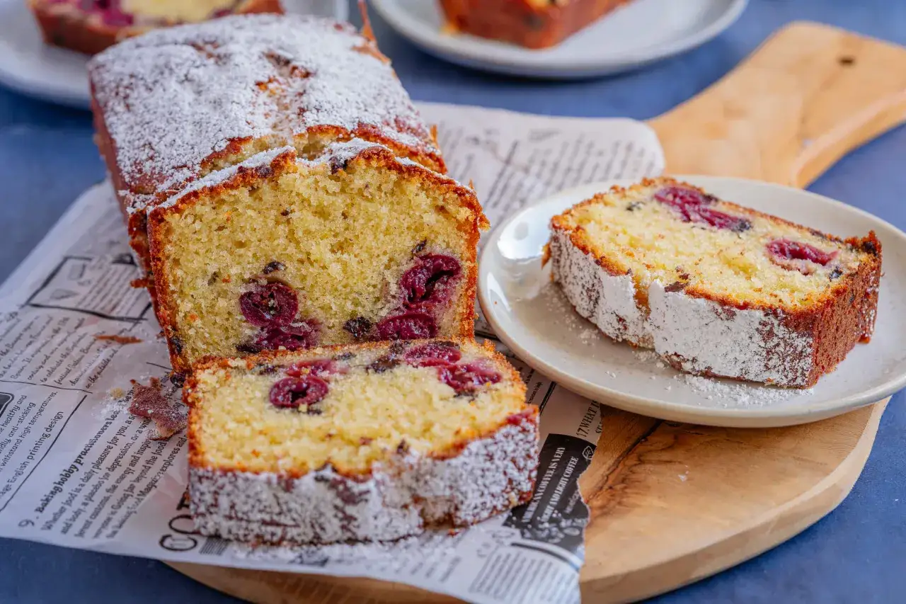Kuchen backen mit Zutaten, die man immer im Haus hat: saftiger Kirschkuchen mit Puderzucker best&auml;ubt, auf Zeitungspapier und Holzbrett serviert.