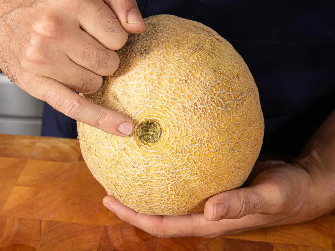 Eine Hand zeigt auf die Cantaloupe Melone mit ihrer typischen Netzstruktur.