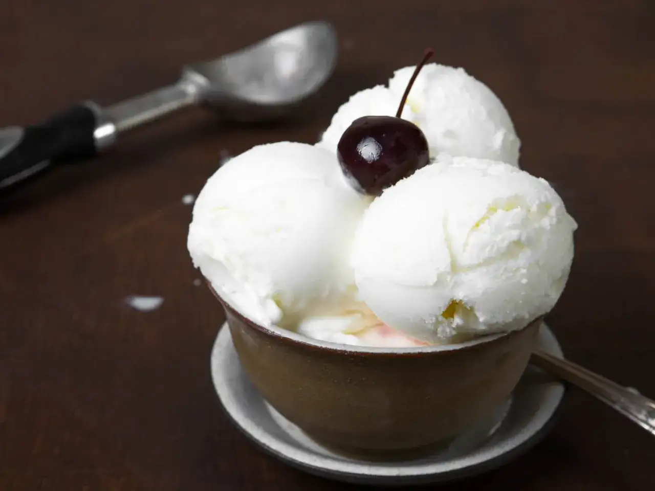 Cremiges griechischer joghurt eis ohne eismaschine, garniert mit einer Kirsche, serviert in einer Schale. Ein L&ouml;ffel liegt daneben.