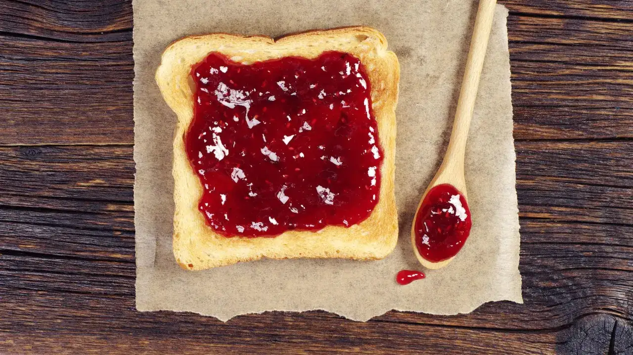 Geröstetes Brot mit leckerer Marmelade, die aussieht, als wäre sie mit Gelierzucker selber gemacht. Eine Holzlöffel liegt daneben.