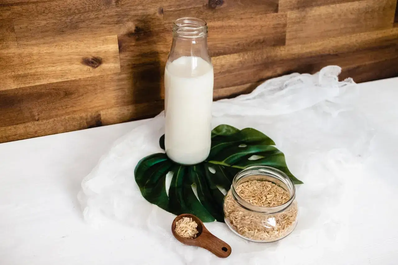Flasche mit selbstgemachter Reismilch, daneben ein Glas Reis und ein L&ouml;ffel. Zutaten f&uuml;r Reismilch selber machen.