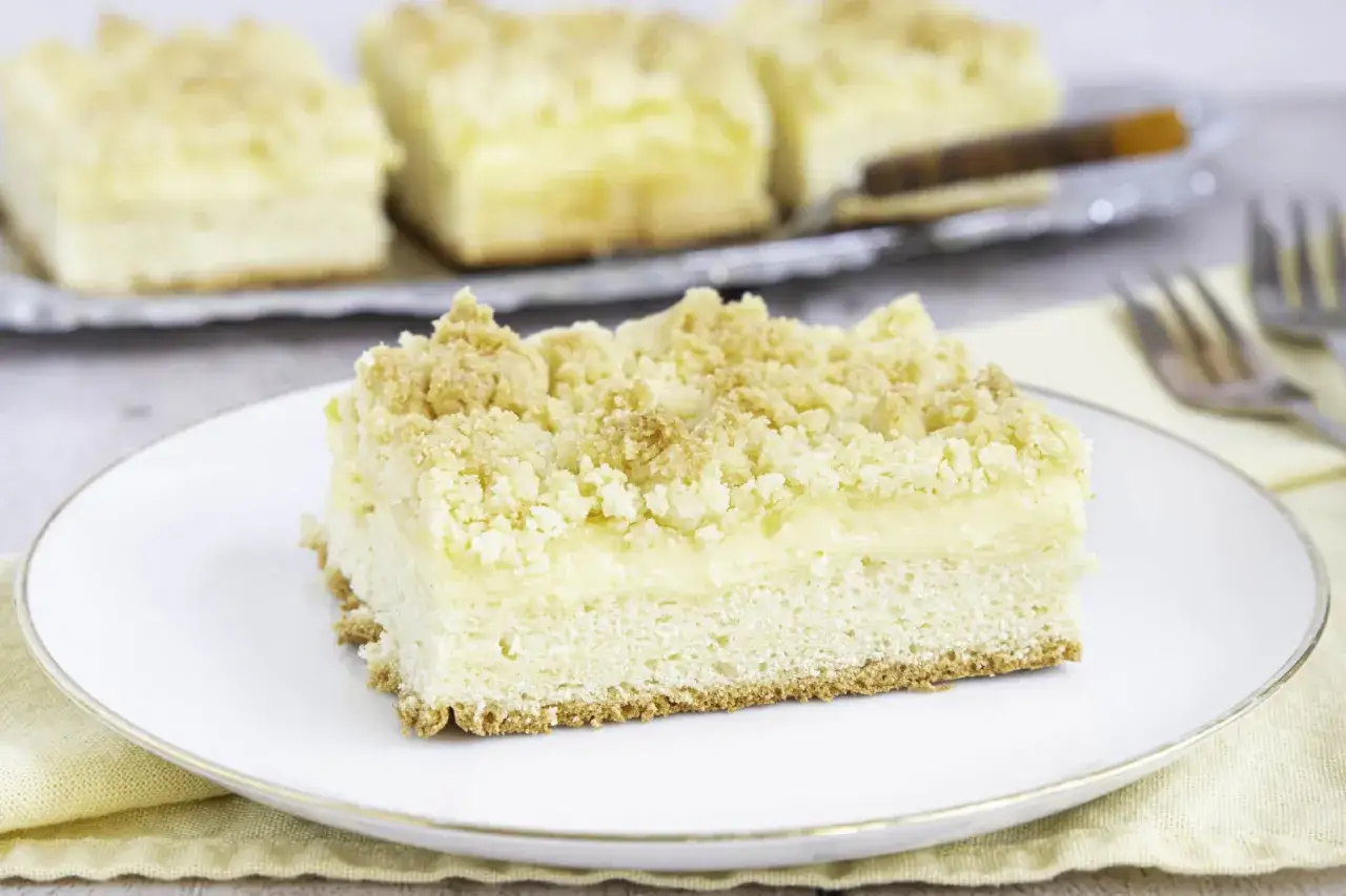 Ein St&uuml;ck Streuselkuchen mit Pudding auf einem Teller, im Hintergrund weitere St&uuml;cke auf einem Blech.