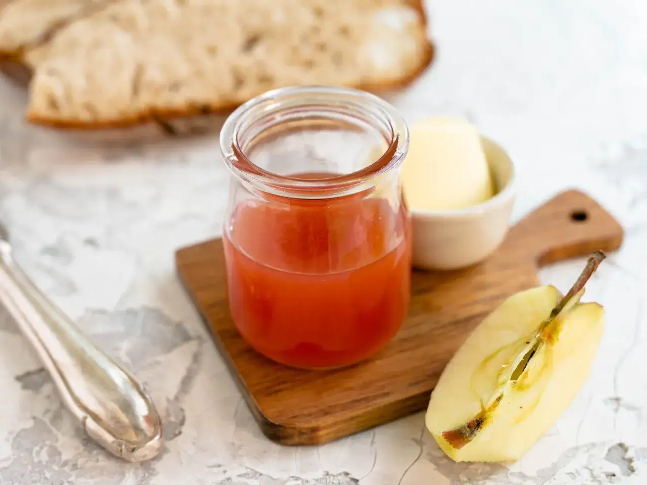 Ein Glas roter Saft, Butter und Apfelspalten auf einem Holzbrett &ndash; eine leckere apfeldicksaft alternative f&uuml;r den Fr&uuml;hst&uuml;ckstisch.