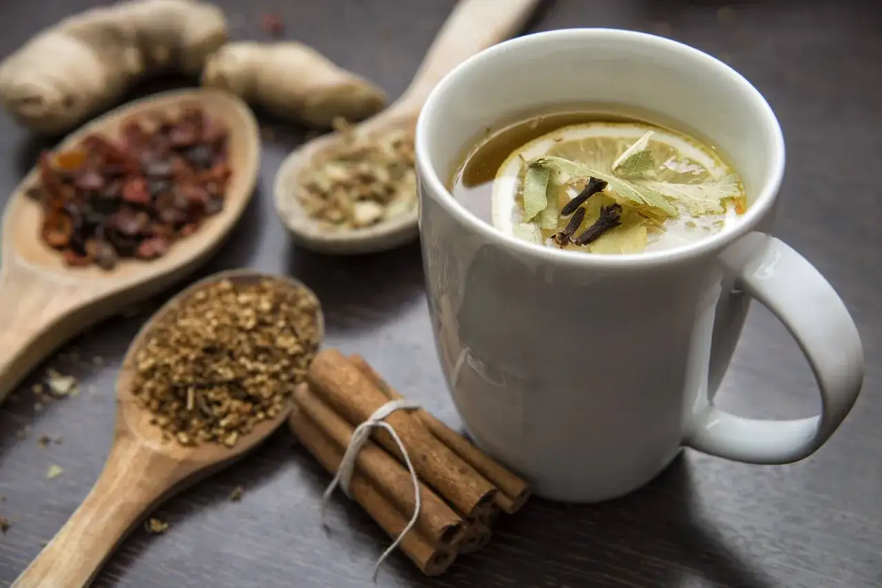 Zutaten f&uuml;r chai selber machen: Ingwer, Zimt, Gew&uuml;rze auf L&ouml;ffeln und eine Tasse mit Tee, Zitrone und Kr&auml;utern.