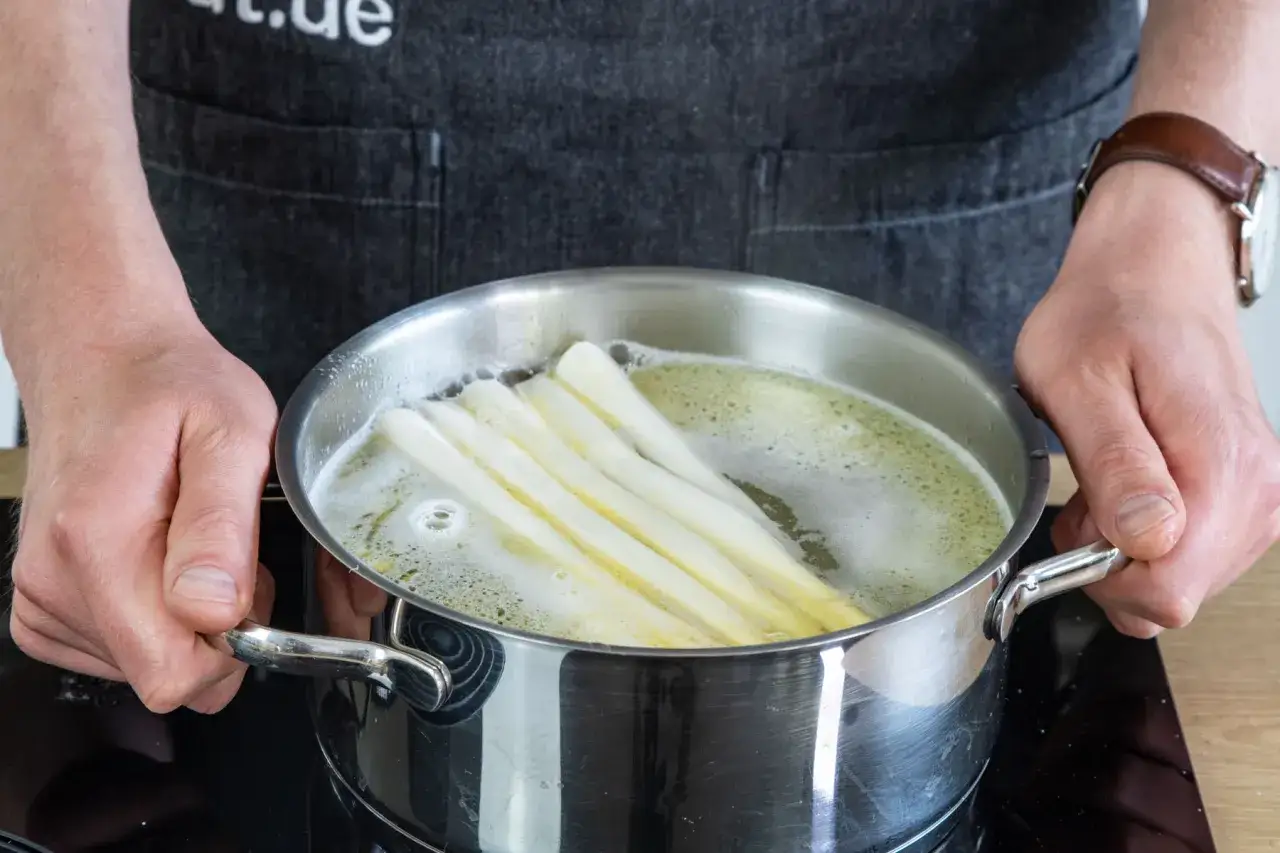 Spargel kochen: Ein Koch h&auml;lt einen Topf mit siedendem Wasser, in dem wei&szlig;er Spargel gart. Ob mit oder ohne Deckel, das Ergebnis ist k&ouml;stlich.