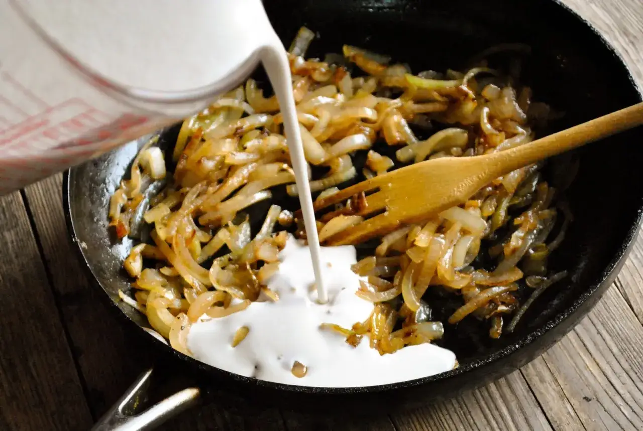 Gebratene Zwiebeln in einer Pfanne, dazu wird eine wei&szlig;e Fl&uuml;ssigkeit gegossen &ndash; der Anfang, um vegane Sahne selber machen.