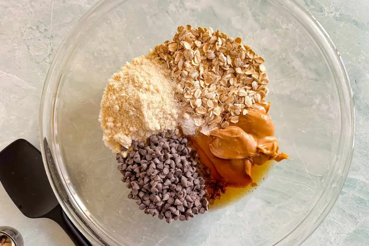 Zutaten für ein einfaches Power Balls Rezept: Haferflocken, Mandelmehl, Schokodrops und Erdnussbutter in einer Schüssel.
