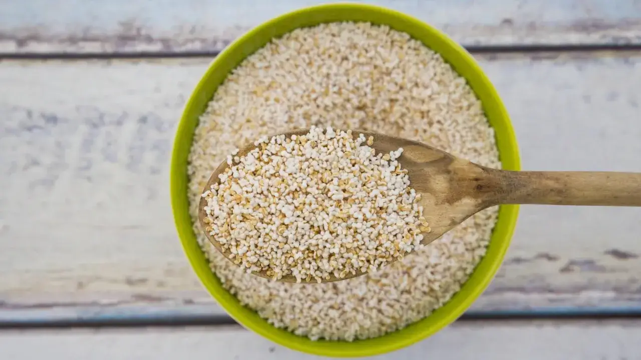Eine Holzschüssel gefüllt mit gepufftem Amaranth, bereit zum Essen. Eine Löffelprobe zeigt die kleinen, luftigen Körner.