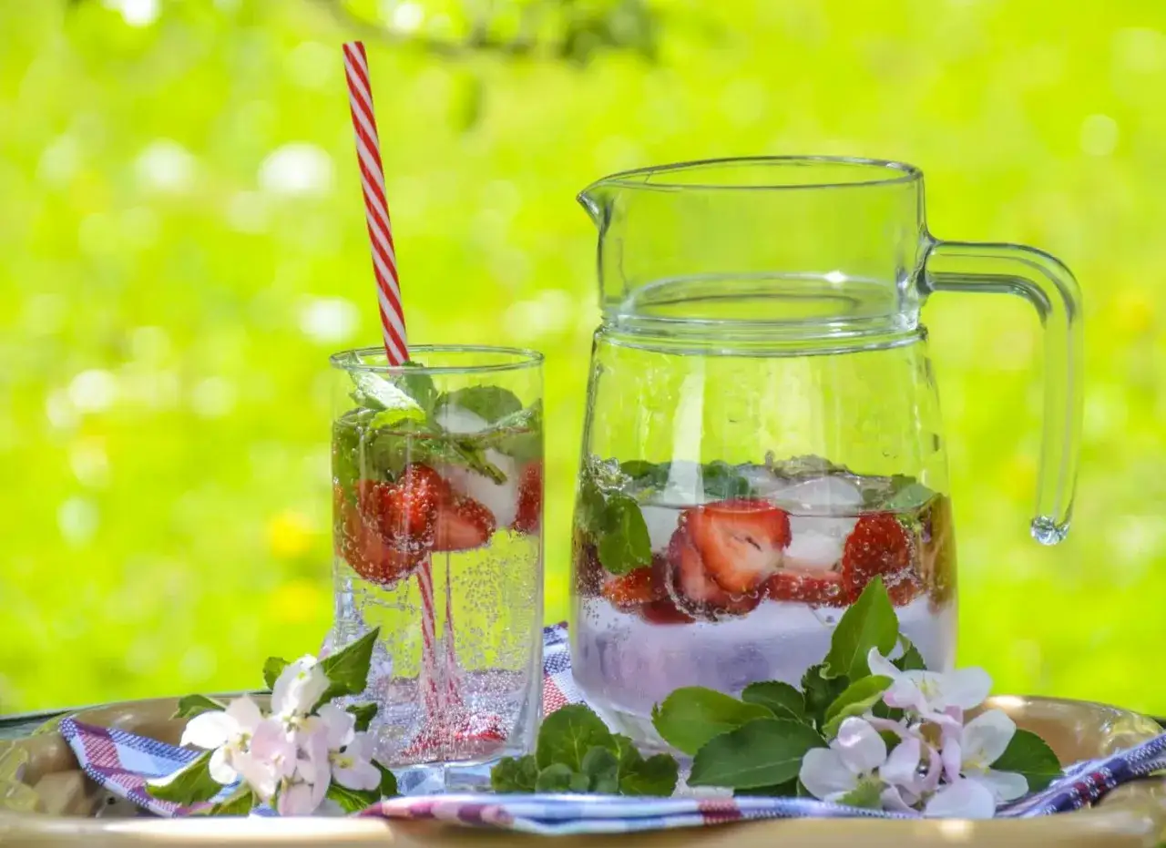 Erfrischendes Erdbeer-Minz-infused Wasser in einem Glas und einer Karaffe, bereit für einen sonnigen Tag im Freien.