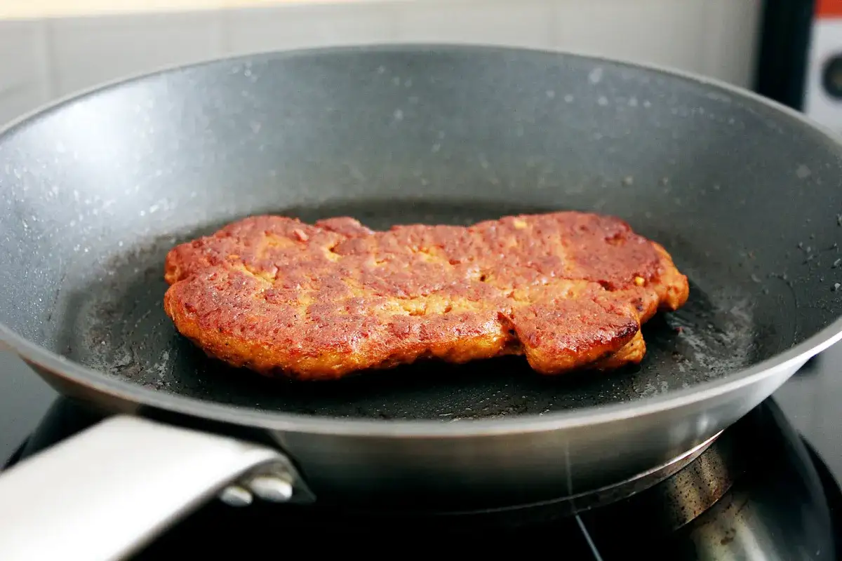 Ein goldbraunes Seitan-Steak br&auml;t in einer Pfanne.