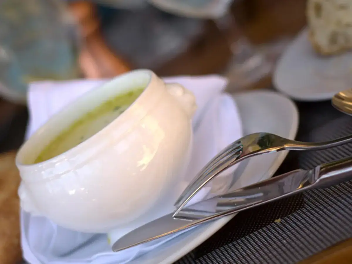 Eine cremige Spargelsuppe, zubereitet aus Spargelschalen, serviert in einer wei&szlig;en Sch&uuml;ssel mit Besteck.
