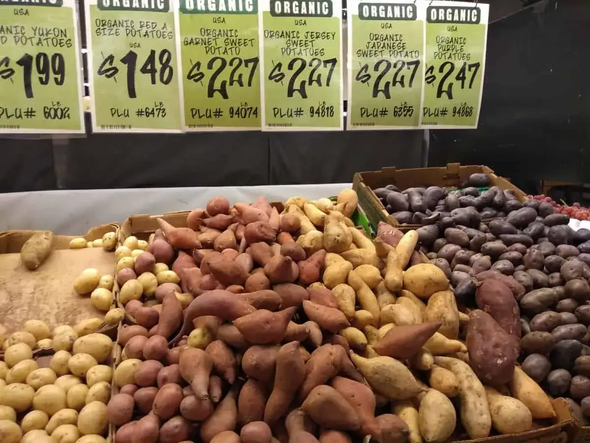 Bunte Auswahl an Bio-Kartoffeln und tropischen S&uuml;&szlig;kartoffeln, darunter Garnet Sweet Potatoes, in Kisten und auf einem Tresen.