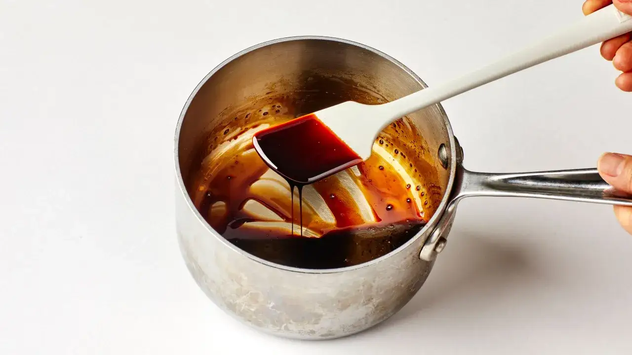 Ein wei&szlig;er Spatel hebt dickfl&uuml;ssige, dunkle Balsamico-Creme aus einem Topf. So einfach l&auml;sst sich Balsamico Creme selber machen!
