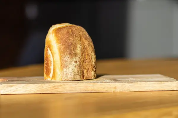 Ein frisch gebackenes Brot liegt auf einem Holzbrett. Die Kruste ist goldbraun und knusprig, was zeigt, wie wird brot saftig.