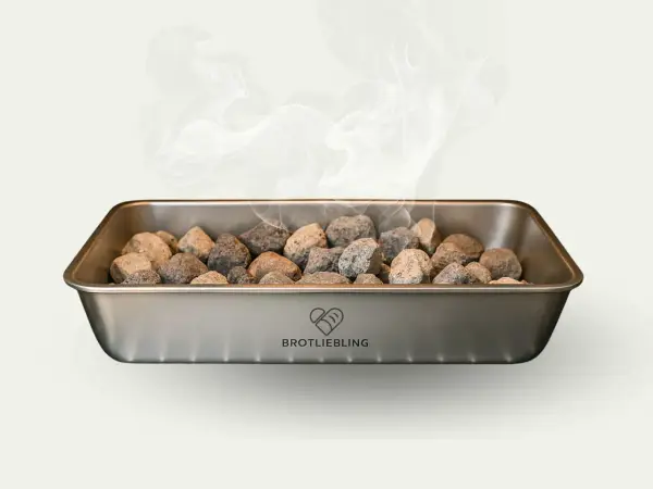 Dampf steigt aus einem Metallbehälter mit Steinen auf. Für knuspriges Brot muss man Wasser in den Ofen geben.